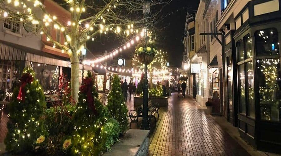 A festive street decorated with lights and holiday greenery at night.