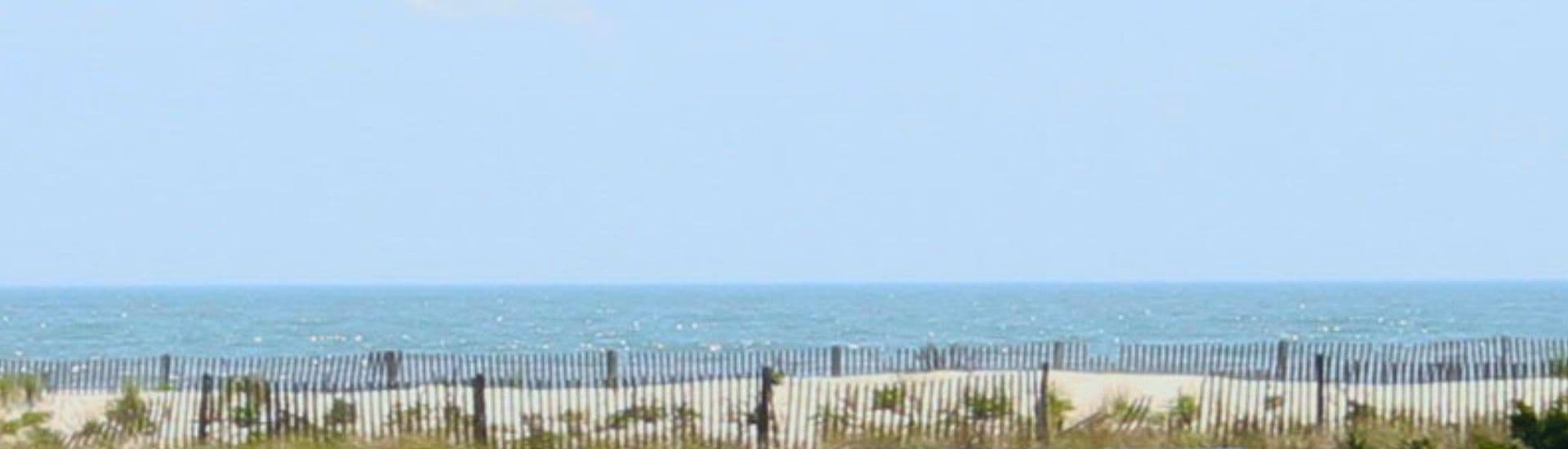 A tranquil view of the ocean with sand dunes and a fence in the foreground.
