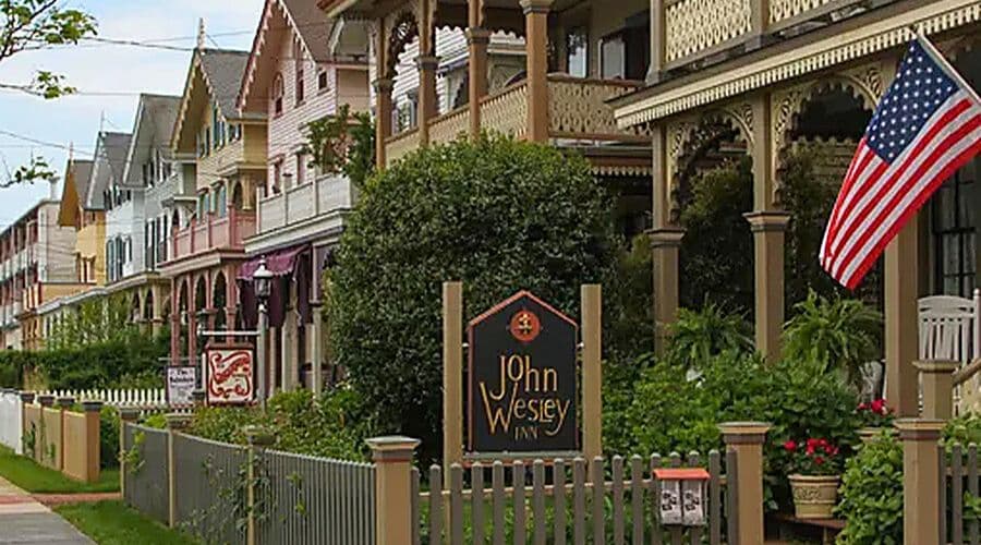 A picturesque row of pastel-colored Victorian houses with a sign for the John Wesley Inn and an American flag.